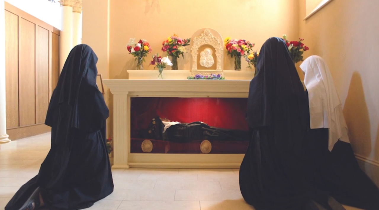 Three sisters kneeling beside Wilhelmina Lancaster’s displayed body.